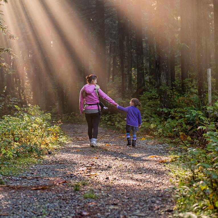 A mom walks on a trail in the forest with her two young kids